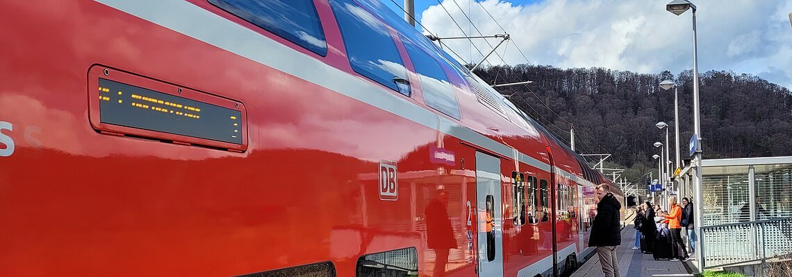 Eine Regionalbahn hat am Gleis gehalten und Reisende warten darauf, dass sich die Türen öffnen.