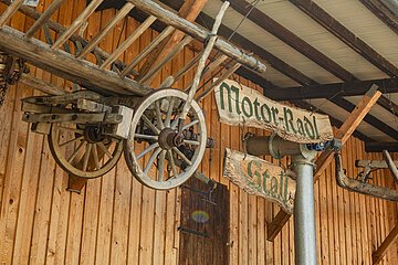 Radangebot in der Krone Kinding Holzwagenrad und Holzschilder mit der Aufschrift "Motor-Radl Stall" an einer Holzwand.