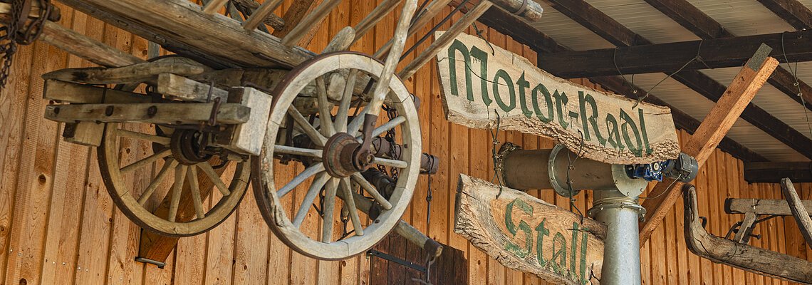 Radangebot in der Krone Kinding Holzwagenrad und Holzschilder mit der Aufschrift "Motor-Radl Stall" an einer Holzwand.