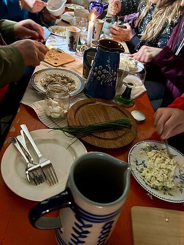 Menschen bereiten an einem gedeckten Tisch mit Kerze und Keramikgeschirr Speisen zu.