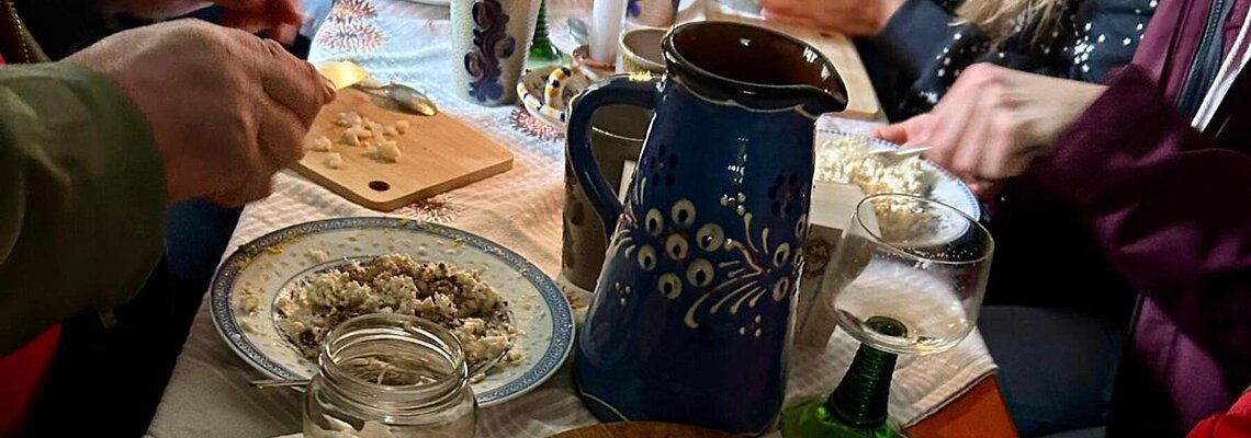 Menschen bereiten an einem gedeckten Tisch mit Kerze und Keramikgeschirr Speisen zu.