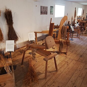 Historische Flachsbearbeitungsgeräte und gebündelte Flachspflanzen in einem Museum mit Holzboden.