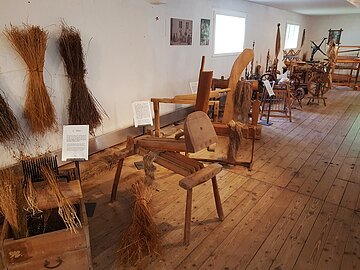Historische Flachsbearbeitungsgeräte und gebündelte Flachspflanzen in einem Museum mit Holzboden.