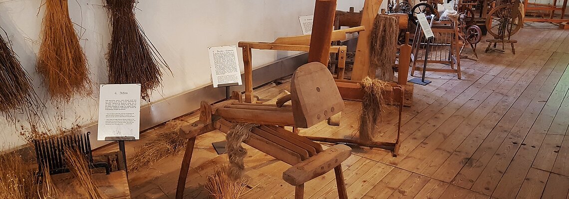 Historische Flachsbearbeitungsgeräte und gebündelte Flachspflanzen in einem Museum mit Holzboden.